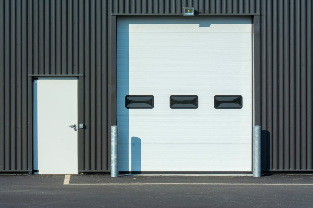 A modern industrial warehouse facade with a large white garage door and side entrance.